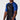 Someone wearing the FUJI x Alliance Ranked Short Sleeve Rashguard Blue, featuring a fitted design, blue short sleeves, a black front, and a white stylized wave and triangle logo on the chest. The background is plain white.
