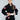 A young girl smiles as she models the Kids Competition BJJ Gi Black, featuring red and white patches and a white belt, against a plain gray background.