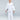 A boy smiles barefoot on a white floor, wearing the All Around Kids BJJ Gi White with a white belt and Gracie Barra sleeve patch, against a plain light gray background.
