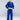 A young boy wears the Kids Competition BJJ Gi Blue with a white belt, standing barefoot on a light floor and looking at the camera with a neutral expression.