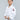 A young boy, smiling, stands against a plain background wearing the All Around Kids BJJ Gi White with the FUJI kimono logo on his sleeve and holding his uniform belt.