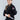 A young girl confidently smiles at the camera wearing the All Around Kids BJJ Gi Black and holding a white belt, set against a plain gray background.