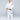 A boy stands barefoot on a white floor, smiling and holding his black belt while wearing the Kids Competition BJJ Gi White with red patches.
