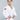 A young boy in a Kids Competition BJJ Gi White with red patches stands confidently against a plain gray background, gazing to the side while adjusting his belt.