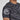 A person wears the Battle Flex Lite Rashguard Black, a short-sleeve athletic shirt with abstract black and gray patterns and a mountain logo on the sleeve, shown in a close-up of the shoulder and upper arm.