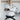 A man in the All Around BJJ Gi White with a black belt stands with arms crossed before a wall displaying the Fuji Mats logo.
